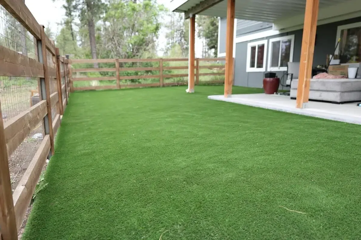Backyard patio area with fresh artificial grass installation near a fenced yard.