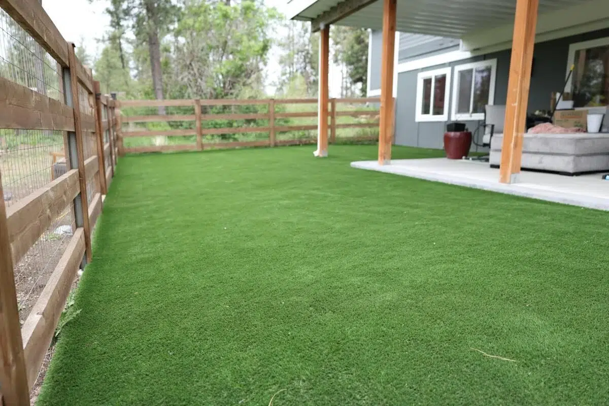 Backyard patio area with fresh artificial grass installation near a fenced yard.