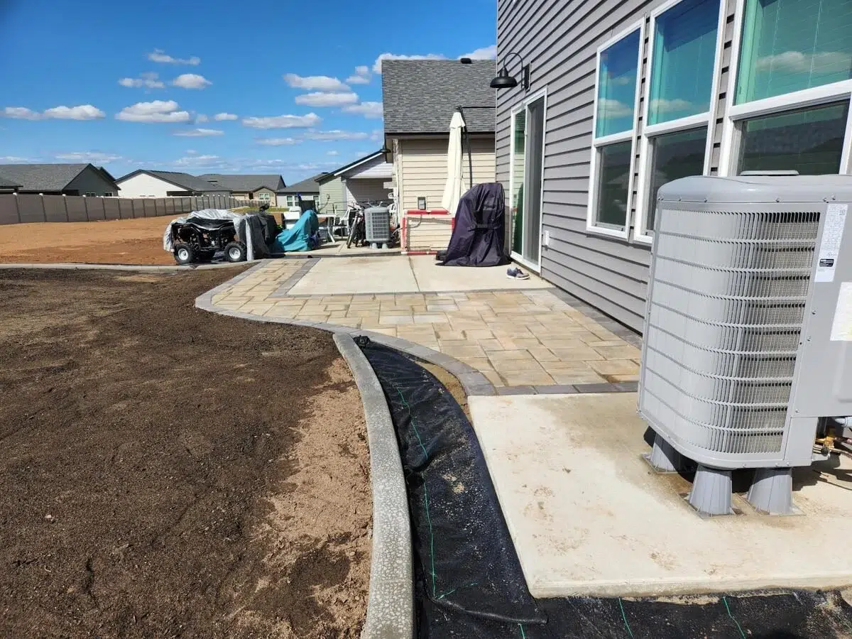 Preparation site for sprinkler system installation with edging and groundwork laid beside a home.