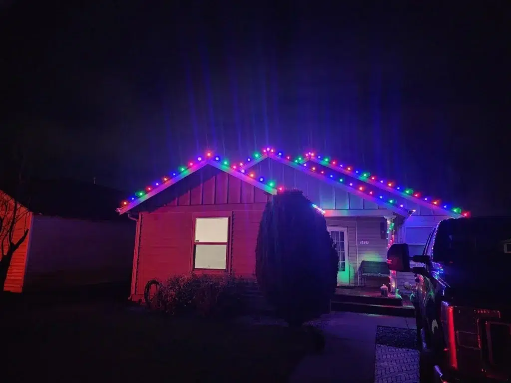Spokane house with multicolor LED Christmas lights installed by Greenscape Landscaping, glowing blue and pink.